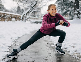 A woman in workout gear stretches on a winter day.