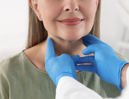 The gloved hands of a health professional check a woman’s throat for signs of thyroid issues.