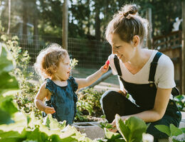 A woman and a toddler kneel in a garden.