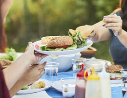 A woman at a family picnic adds salad to a plate of food.