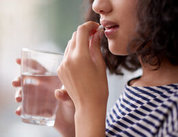 A woman takes a pill with a glass of water.