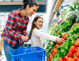 A mother and daughter choose bell peppers at a grocery store.